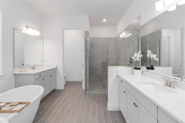 full bath with wood finish floors, toilet, two vanities, a stall shower, and a sink