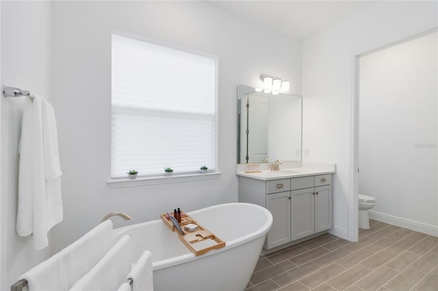 bathroom featuring toilet, vanity, baseboards, and a freestanding tub