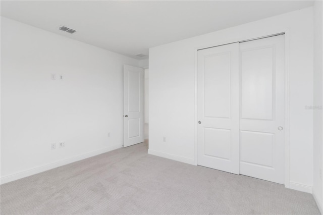 unfurnished bedroom featuring visible vents, baseboards, light colored carpet, and a closet