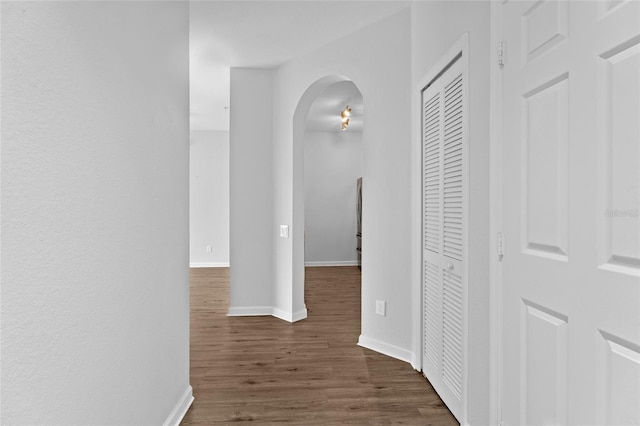 hall with arched walkways, dark wood-style floors, and baseboards