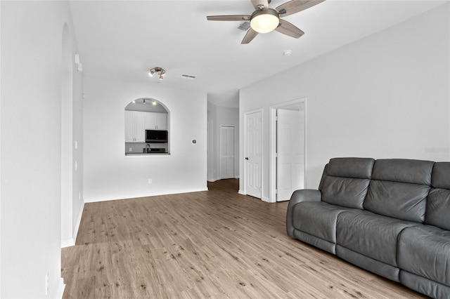 living room with arched walkways, visible vents, light wood-style flooring, and a ceiling fan