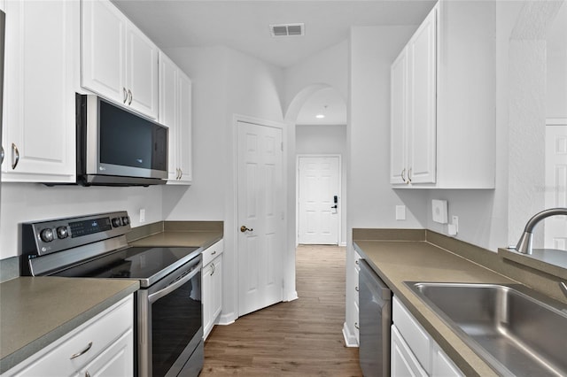 kitchen with stainless steel appliances, dark countertops, white cabinets, and a sink