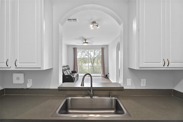 kitchen with dark countertops, white cabinets, a sink, and arched walkways