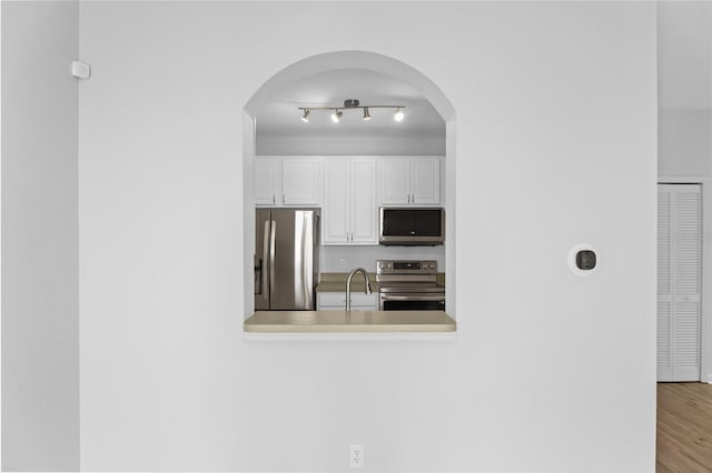 kitchen featuring light countertops, appliances with stainless steel finishes, white cabinetry, a sink, and wood finished floors