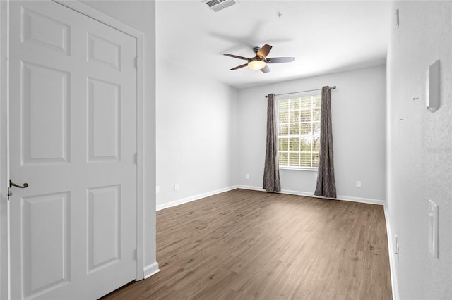 spare room with dark wood-style floors, a ceiling fan, visible vents, and baseboards