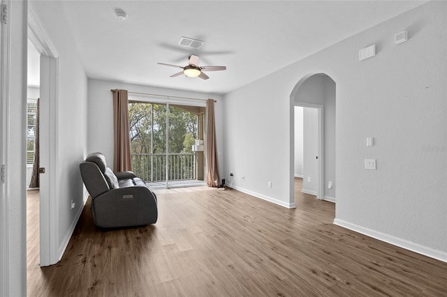 living area featuring baseboards, visible vents, arched walkways, ceiling fan, and wood finished floors