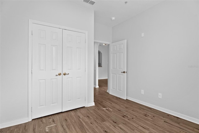 unfurnished bedroom with arched walkways, a closet, visible vents, wood finished floors, and baseboards