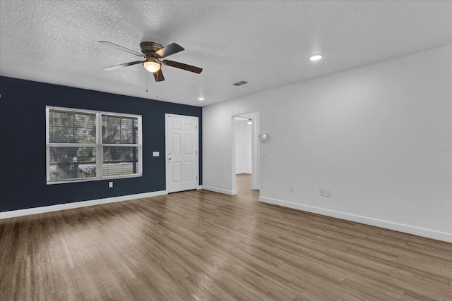 unfurnished room featuring light wood-type flooring, visible vents, a textured ceiling, and baseboards