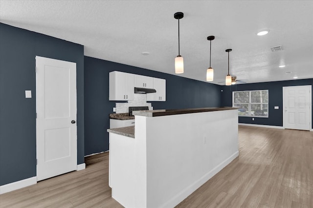 kitchen featuring dark countertops, hanging light fixtures, open floor plan, white cabinets, and under cabinet range hood