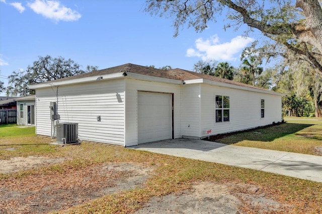 view of side of home featuring concrete driveway, a lawn, an attached garage, and cooling unit