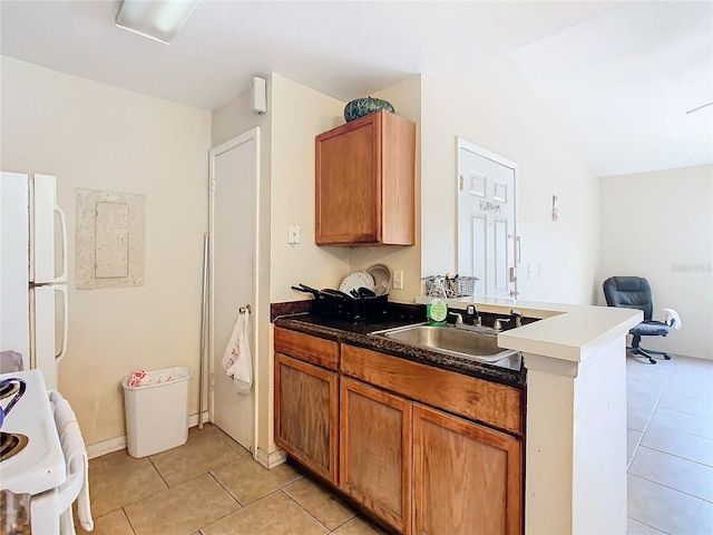 kitchen with light tile patterned floors, white appliances, a sink, brown cabinets, and dark countertops