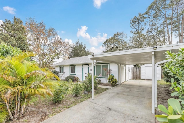 view of front of house with a storage unit, concrete driveway, fence, a carport, and an outdoor structure