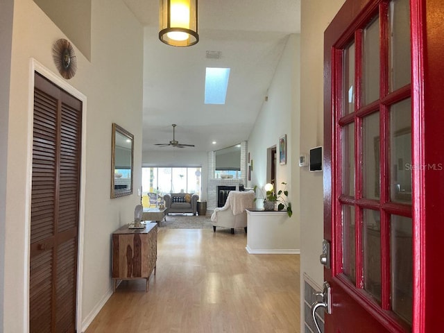 foyer entrance featuring baseboards, visible vents, a ceiling fan, light wood-type flooring, and a brick fireplace