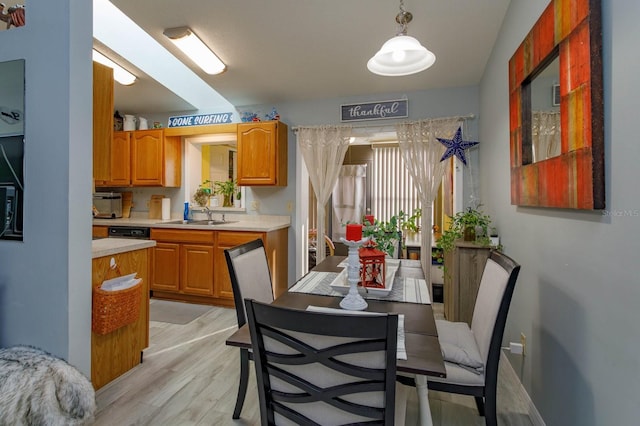 kitchen with a sink, light wood-style floors, light countertops, brown cabinetry, and pendant lighting