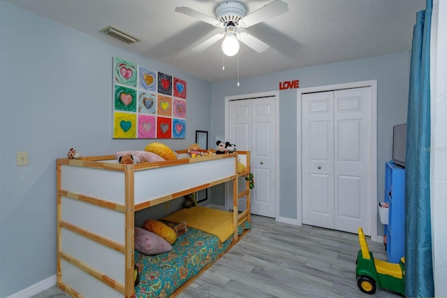 bedroom with two closets, visible vents, ceiling fan, wood finished floors, and baseboards