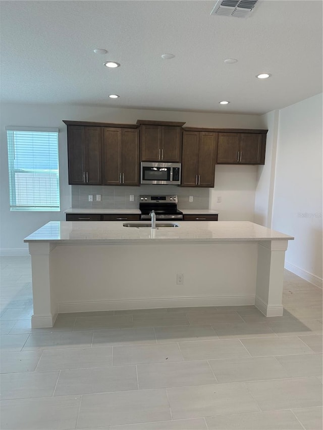 kitchen with stainless steel appliances, light countertops, visible vents, and an island with sink