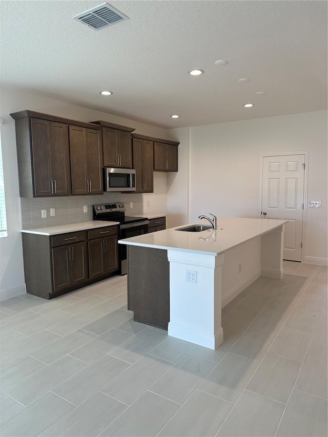 kitchen with a kitchen island with sink, a sink, visible vents, light countertops, and appliances with stainless steel finishes