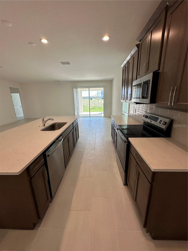 kitchen with recessed lighting, a sink, appliances with stainless steel finishes, backsplash, and a center island with sink