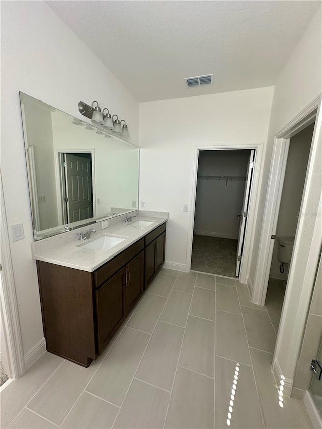 bathroom featuring a walk in closet, visible vents, a sink, and double vanity