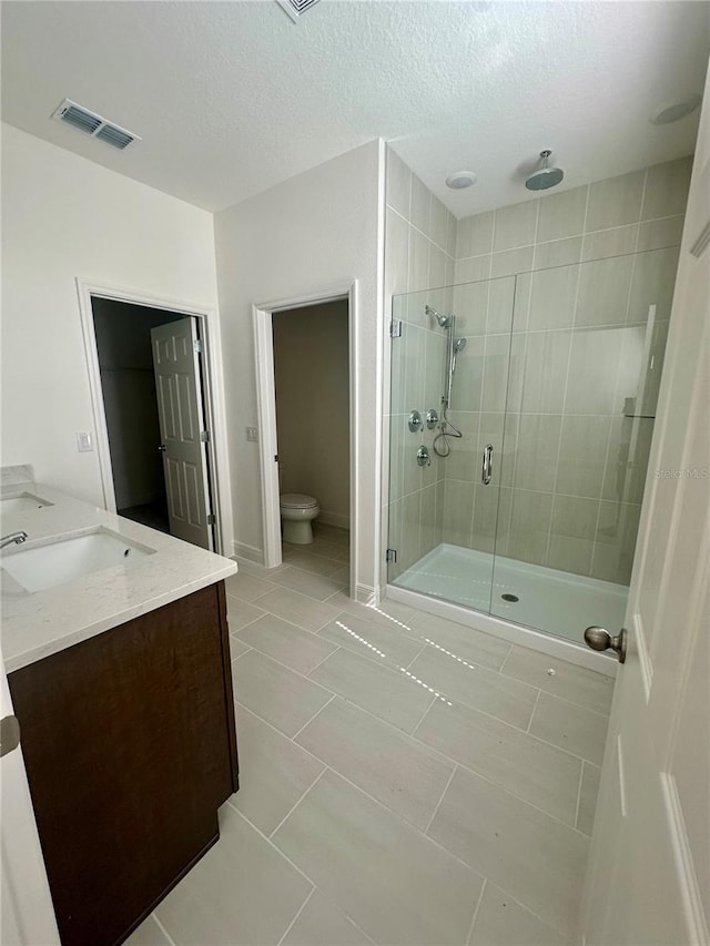 bathroom featuring double vanity, visible vents, toilet, a shower stall, and a sink