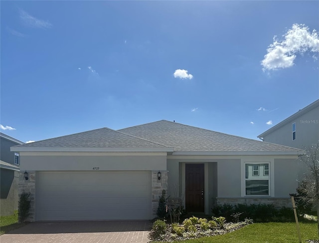 ranch-style house with stone siding, roof with shingles, an attached garage, decorative driveway, and stucco siding