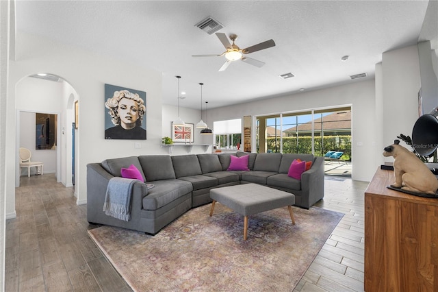 living area featuring arched walkways, visible vents, a textured ceiling, and wood finished floors