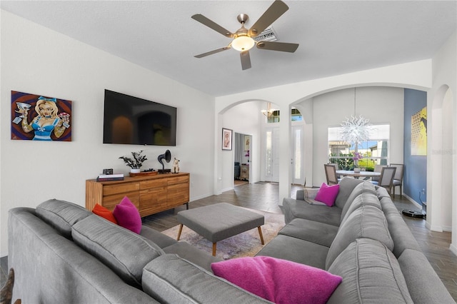 living area with arched walkways, ceiling fan with notable chandelier, and baseboards