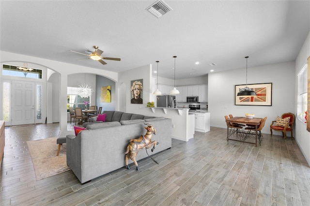 living room featuring arched walkways, recessed lighting, visible vents, light wood-style flooring, and an inviting chandelier