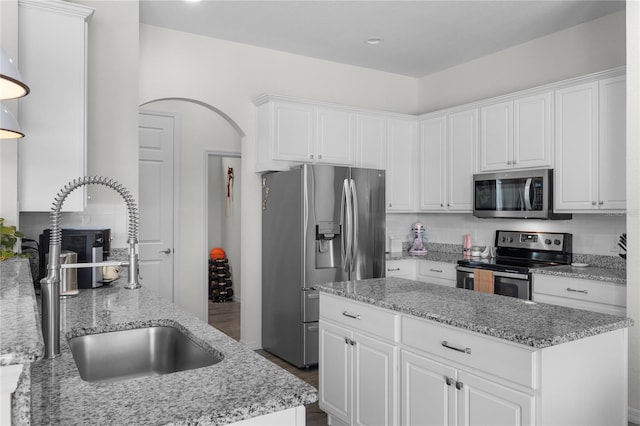 kitchen featuring arched walkways, a center island, stainless steel appliances, white cabinetry, and a sink