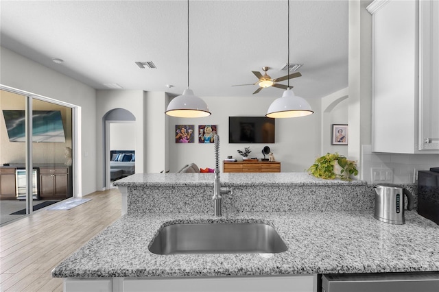 kitchen featuring light stone counters, visible vents, white cabinetry, a sink, and light wood-type flooring