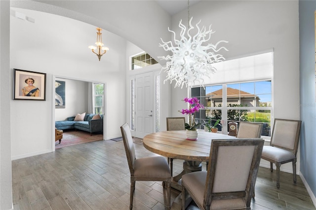 dining space featuring a high ceiling, a healthy amount of sunlight, wood finished floors, and a notable chandelier