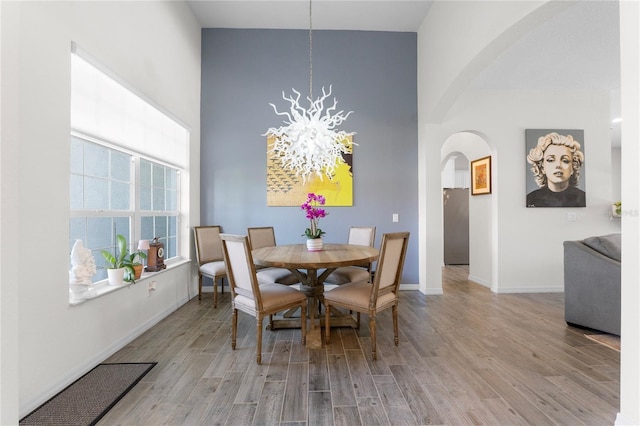 dining room featuring baseboards, arched walkways, a towering ceiling, wood finished floors, and an inviting chandelier