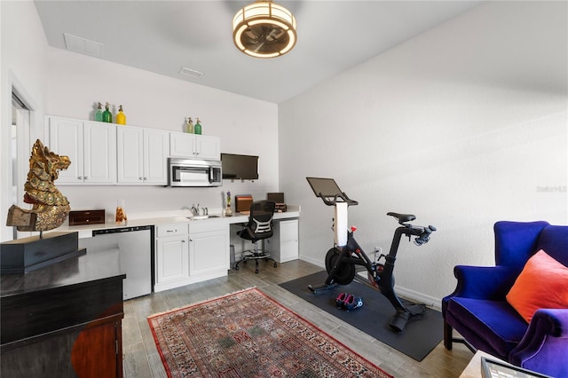 office featuring baseboards, visible vents, built in study area, light wood-style flooring, and a sink