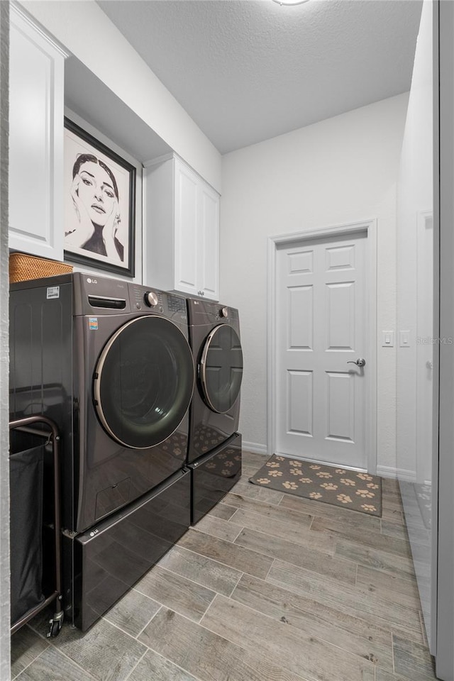 washroom featuring a textured ceiling, baseboards, cabinet space, wood tiled floor, and washer and clothes dryer