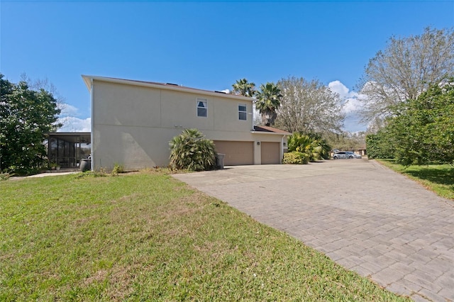 view of side of property with an attached garage, a lawn, decorative driveway, and stucco siding