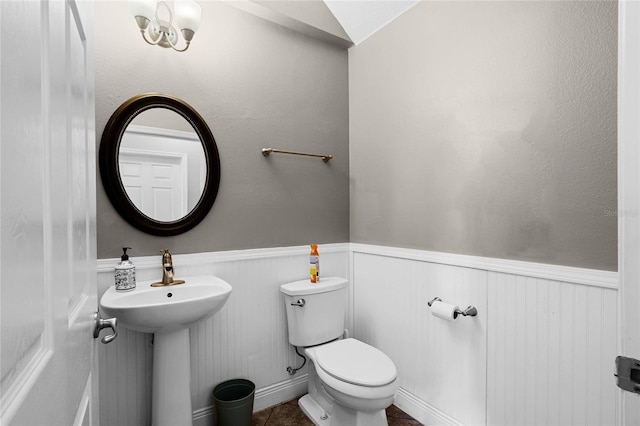 half bath featuring tile patterned flooring, wainscoting, a sink, and toilet