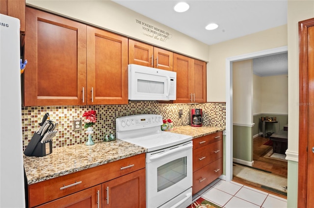 kitchen with decorative backsplash, brown cabinetry, light tile patterned flooring, light stone countertops, and white appliances