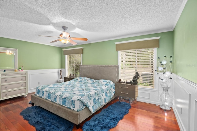 bedroom featuring dark wood-style floors, ornamental molding, a wainscoted wall, and a textured ceiling