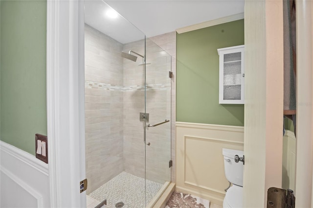 full bathroom with wainscoting, a shower stall, toilet, and a decorative wall