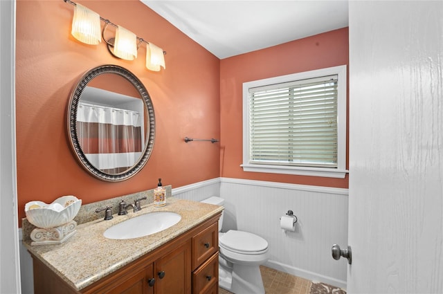 full bath featuring toilet, vanity, and wainscoting