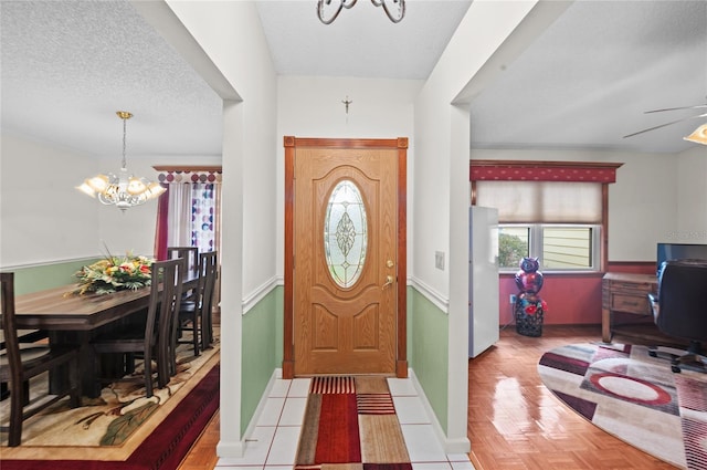 foyer entrance featuring a textured ceiling, ceiling fan with notable chandelier, and baseboards