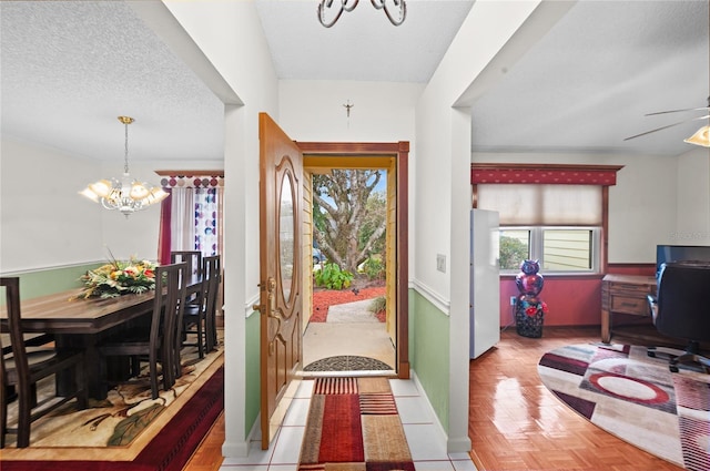 foyer entrance featuring a textured ceiling, ceiling fan with notable chandelier, and baseboards