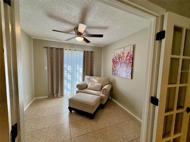 living area with a textured ceiling, baseboards, a ceiling fan, and light tile patterned flooring