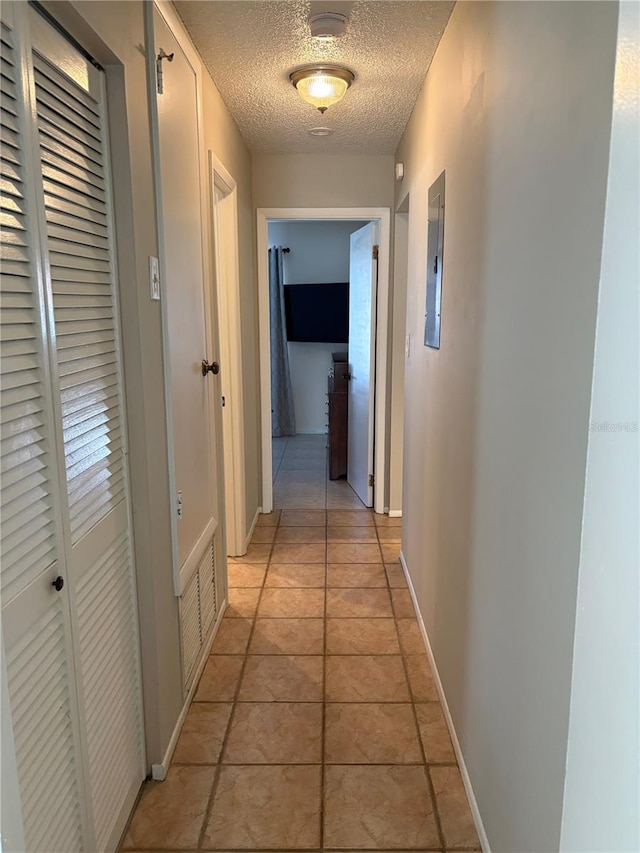 hall featuring light tile patterned floors, electric panel, baseboards, and a textured ceiling