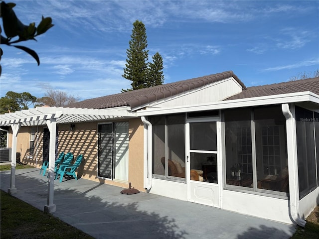 view of side of home featuring a sunroom, a tiled roof, a patio area, a pergola, and stucco siding