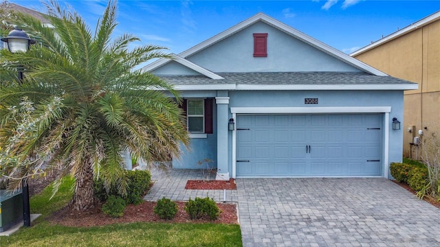 single story home with a garage, decorative driveway, roof with shingles, and stucco siding