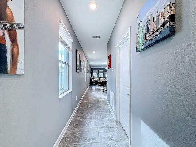 hallway with stone finish floor, recessed lighting, visible vents, and baseboards