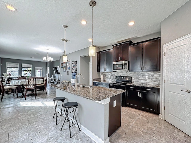 kitchen with pendant lighting, stainless steel microwave, a sink, dark stone countertops, and an island with sink