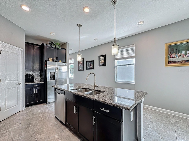 kitchen featuring a kitchen island with sink, a sink, hanging light fixtures, appliances with stainless steel finishes, and light stone countertops