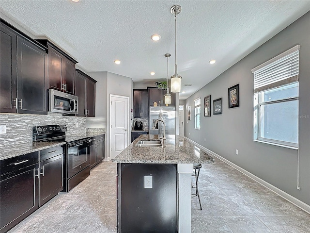 kitchen featuring decorative light fixtures, stainless steel appliances, a sink, backsplash, and a center island with sink